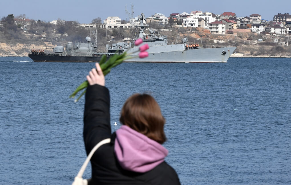 Девушка машет с набережной военному кораблю в Севастополе.
